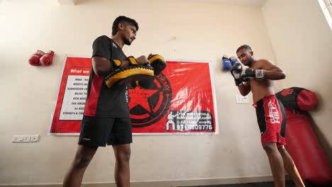 Bengaluru-Karnataka--India--February-13-2020-Looking-up-shot-of-a-professional-mixed-martial-arts-fighter-doing-round-house-spinning-back-kick-and-another-fighter-holding-the-pads