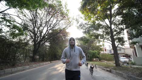 Closeup-of-an-adult-asian-man-wearing-a-hoodie-sweat-shirt-jogging-with-a-pack-of-dogs-during-dawn