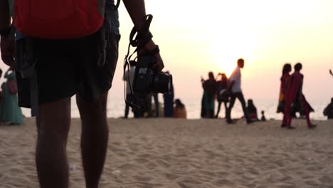 Medium-closeup-of-a-man-wearing-shots-walking-with-a-DSLR-camera-on-a-beach-during-sunset