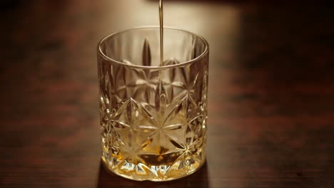 Closeup-moody-view-of-a-person-putting-ice-cubes-and-pouring-whiskey-into-a-glass