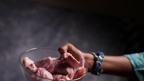 Slow-motion-closeup-view-of-fresh-chicken-wings-falling-from-a-small-glass-bowl-into-a-bigger-glass-bowl