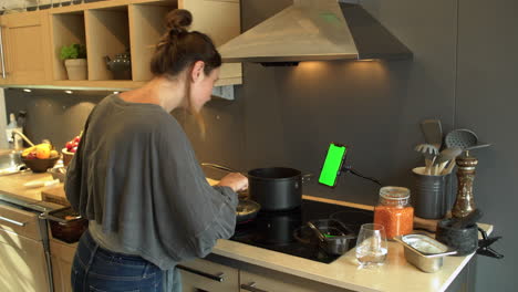 Young-Woman-Cooking-Whilst-Looking-at-Phone-Green-Screen