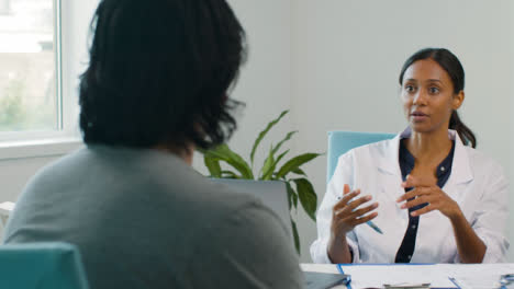 Female-Doctor-Sits-Backs-in-Chair-Talking-to-Patient