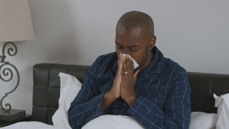 Middle-Aged-Man-Feeling-Ill-In-Bed-Uses-a-Tissue-and-Blows-His-Nose