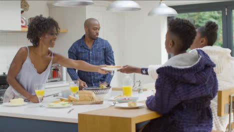 Mother-Hands-Plate-of-Toast-to-Young-Daughter-During-Family-Breakfast