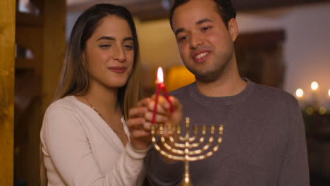 Medium-Shot-of-Young-Couple-Lighting-First-Candle-of-Menorah-During-Hanukkah