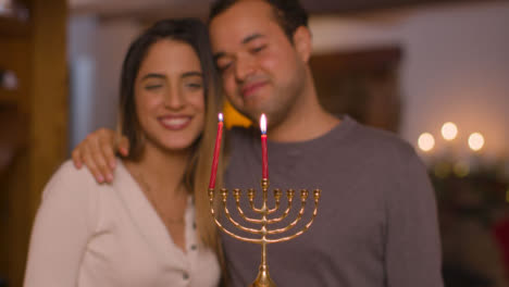 Medium-Shot-of-Young-Couple-Lighting-the-First-Candle-of-Menorah-During-Hanukkah