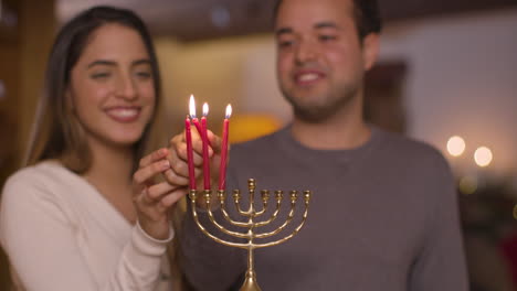 Medium-Shot-of-Young-Couple-Lighting-Three-Candles-of-Menorah-During-Hanukkah