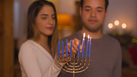 Medium-Shot-of-Young-Couple-Lighting-Candles-On-Menorah-During-Hanukkah