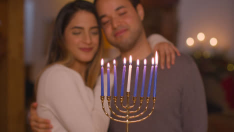 Medium-Shot-of-Young-Couple-Lighting-Candles-On-Menorah-During-Hanukkah-Celebration