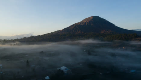 Drone-Shot-Ascending-Over-Low-Hanging-Mist-Around-Mount-Batur-Volcano