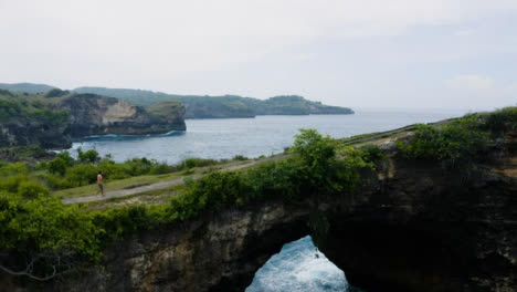 Drone-Shot-Ascending-Over-Person-Walking-Across-Rock-Arch