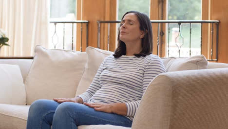 Tracking-Shot-Orbiting-Around-Middle-Aged-Woman-Meditating-On-Sofa