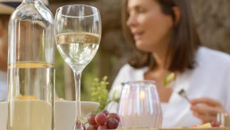 Close-Up-Shot-of-Wine-Bottle-and-Glass-with-Couple-Enjoying-Alfresco-Dinner-In-Background