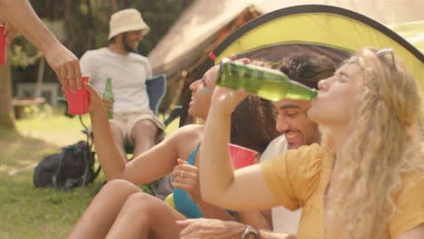 Medium-Shot-of-Young-Festival-Goers-Sitting-Around-as-Friend-Brings-Drinks