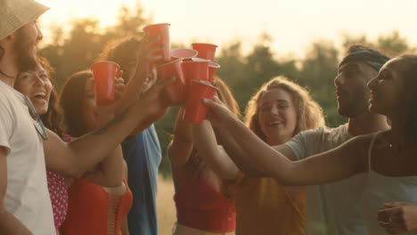 Medium-Shot-of-a-Group-of-Friends-Toasting-Their-Plastic-Beer-Cups-at-Sunset
