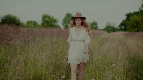 Attractive-Boho-Woman-Walking-On-A-Meadow-In-Summer-Holding-Flowers-In-Hand