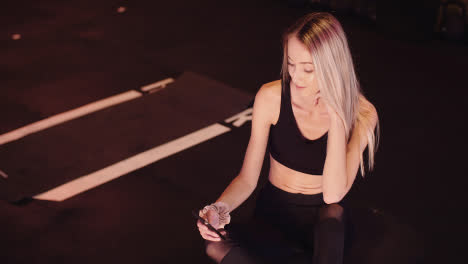 Lockdown-Shot-Of-Young-Woman-Using-Smartphone-While-Relaxing-On-Floor-After-Workout-Session