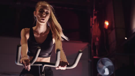 Determined-Young-Woman-Cycling-On-Stationary-Bike-At-Fitness-Studio-1