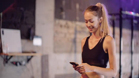 Attractive-Young-Sporty-Woman-Text-Messaging-Through-Mobile-Phone-During-Break-At-Fitness-Club