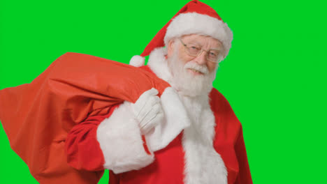 Portrait-Shot-of-Santa-Walking-Into-and-Out-of-Frame-Holding-Sack-with-a-Green-Screen