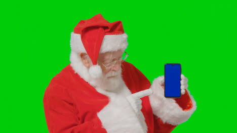 Porträtaufnahme-Des-Weihnachtsmanns,-Der-Ein-Bluescreen-Handy-Vor-Einem-Grünen-Bildschirm-Hält