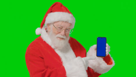 Portrait-Shot-of-Santa-Holding-a-Blue-Screen-Mobile-Phone-In-Front-of-Green-Screen