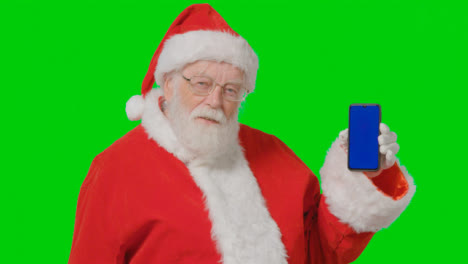 Portrait-Shot-of-Santa-Holding-Blue-Screen-Mobile-Phone-In-Front-of-Green-Screen
