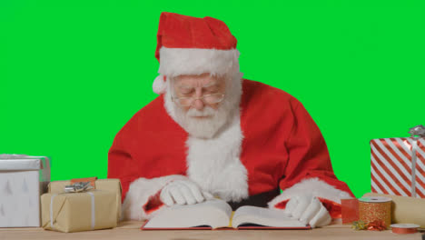 Portrait-Shot-of-Santa-Holding-Reading-Through-Big-Red-Book-Surrounded-by-Presents