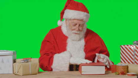 Portrait-Shot-of-Santa-Holding-Reading-Through-a-Big-Red-Book-Surrounded-by-Presents