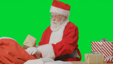 Porträtaufnahme-Des-Weihnachtsmanns,-Der-Geschenke-In-Einen-Sack-Vor-Dem-Grünen-Bildschirm-Legt