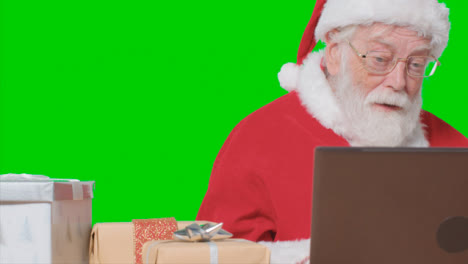 Portrait-Shot-of-Santa-Talking-On-Laptop-Video-Call-In-Front-of-Green-Screen