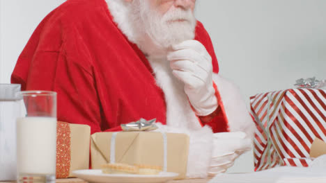 Mittlere-Aufnahme-Des-Weihnachtsmanns,-Der-Am-Schreibtisch-Sitzt-Und-Geschenk-Vorbereitet