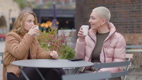 Tracking-Shot-of-Two-Young-Women-Sitting-at-Outdoor-Table-Drinking-Coffee