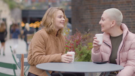 Tracking-Shot-of-Two-Young-Women-Sitting-at-an-Outdoor-Table-Drinking-Coffee