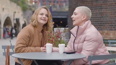Tracking-Shot-of-Two-Young-Women-Sitting-at-an-Outdoor-Table-Drinking-Some-Coffee