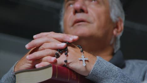 Low-Angle-Shot-of-Senior-Man-Praying-with-Rosary-Beads-and-Bible