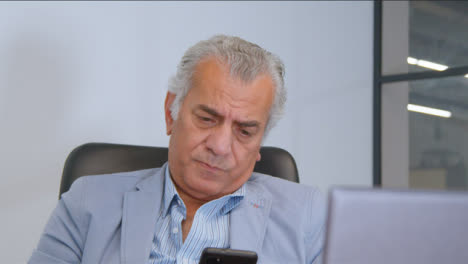 Close-Up-Shot-of-a-Senior-Man-at-a-Desk-On-His-Mobile-Phone