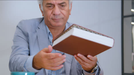Flachwinkelaufnahme-Eines-älteren-Mannes,-Der-Ein-Buch-An-Seinem-Schreibtisch-Liest