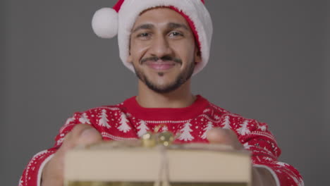 Portrait-Shot-of-Young-Man-Presenting-Christmas-Gift-to-Camera