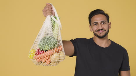 Mid-Shot-of-Young-Man-Holding-Up-Bag-of-Vegetables-and-Smiling
