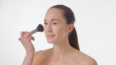 Tracking-Shot-of-a-Young-Woman-Applying-Bronzer-and-Smiling-with-Copy-Space