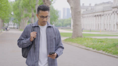Tracking-Shot-of-Young-Man-Walking-Whilst-Looking-at-His-Smartphone