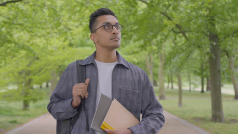 Tracking-Shot-of-Young-Man-Walking-Through-Park-with-Notepad