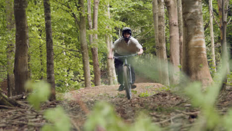 Toma-En-Cámara-Lenta-De-Un-Hombre-En-Bicicleta-De-Montaña-Haciendo-Un-Salto-En-El-Aire-En-Un-Camino-De-Tierra-A-Través-Del-Bosque-4