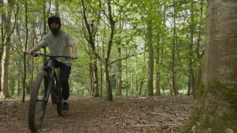 Drone-Tracking-Man-On-Mountain-Bike-Cycling-Doing-Wheelie-Along-Trail-Through-Countryside-And-Woodland