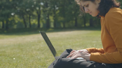 Handheld-Shot-of-Student-Working-and-Typing-On-Laptop-In-a-Park