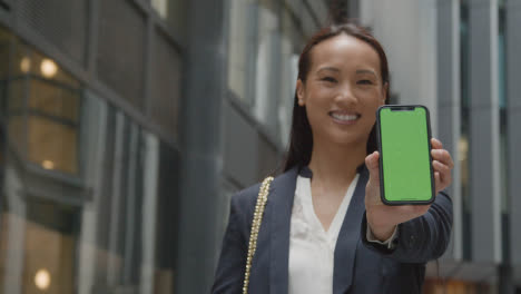 Portrait-Of-Businesswoman-Outside-City-Of-London-Offices-Holding-Up-Green-Screen-Mobile-Phone