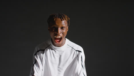 Low-Key-Studio-Portrait-Of-Young-Male-Footballer-Wearing-Club-Kit-Celebrating-Goal-1