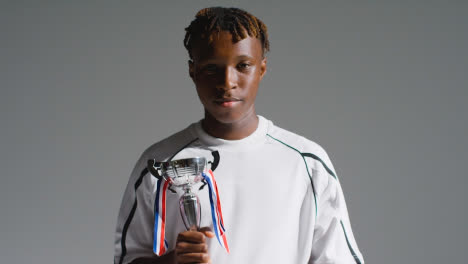 Studio-Portrait-Of-Young-Male-Footballer-Or-Sportsperson-Wearing-Club-Kit-Celebrating-Holding-Trophy-3